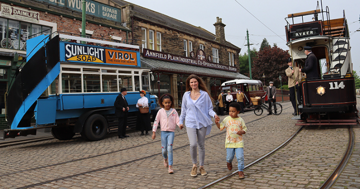 Mother and two children walking at Beamish Museum 1900s Town with Trams in the background.